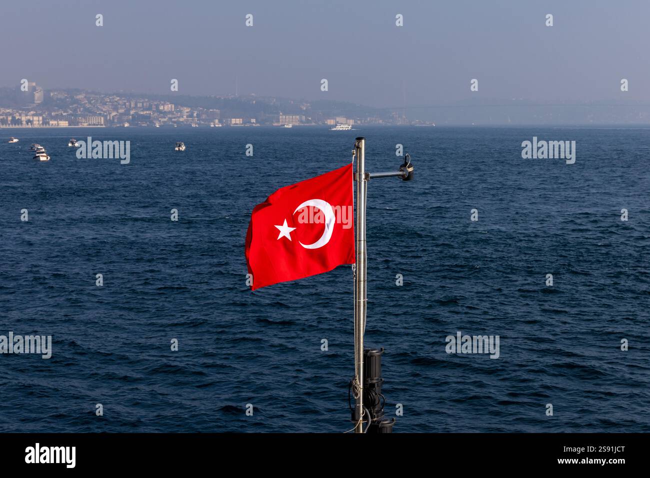 Drapeau turc agitant sur un bateau dans le Bosphore. La mer bleue profonde et le littoral d’Istanbul en arrière-plan créent une scène maritime patriotique Banque D'Images