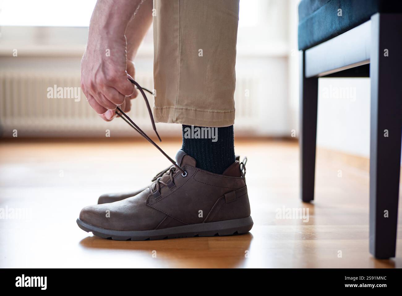 Homme méconnaissable lacant ses chaussures semi-décontractées en cuir marron. Gros plan en angle bas, prise de vue intérieure, lumière naturelle. Banque D'Images