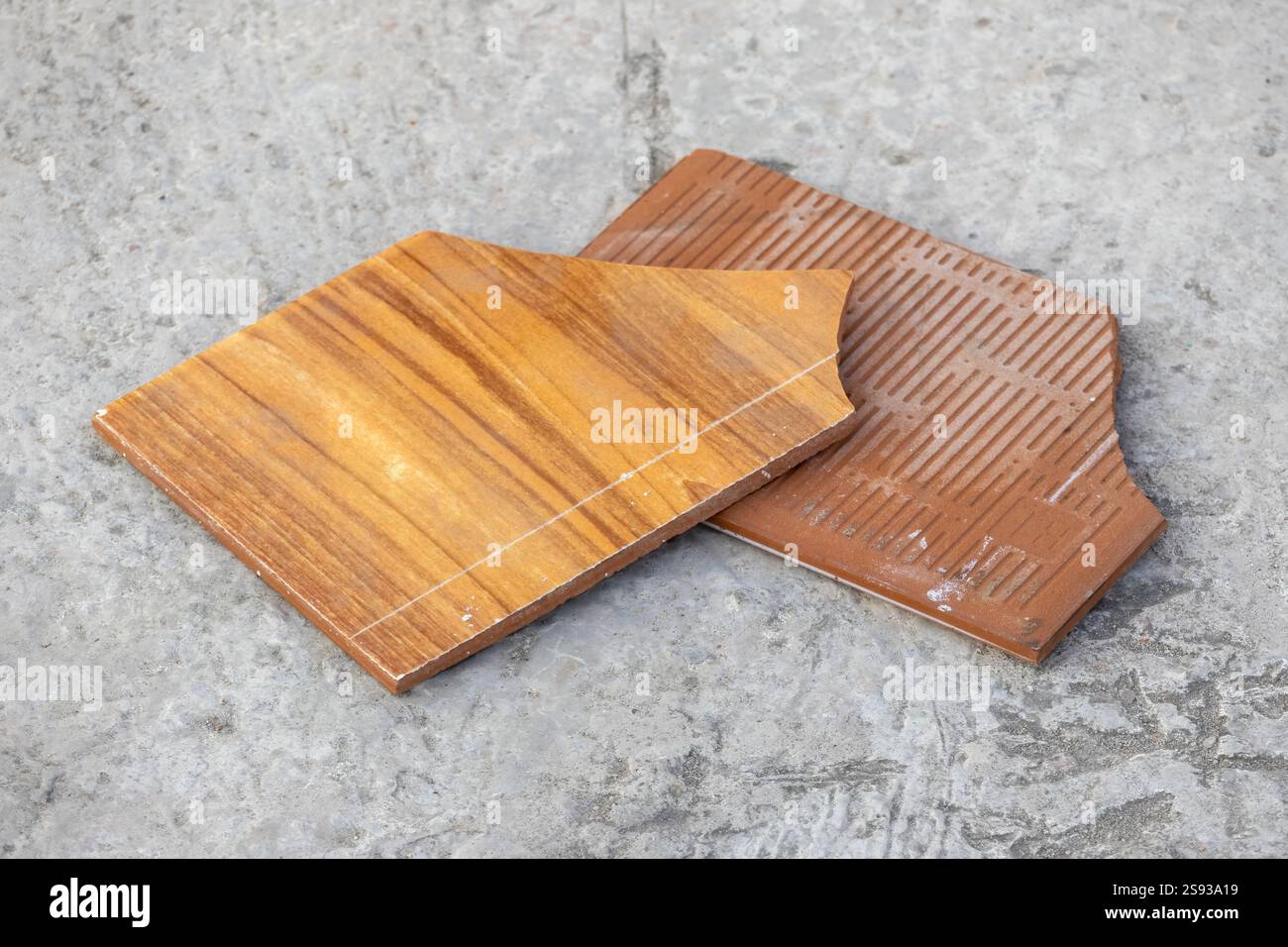 Des fragments de carreaux de céramique cassés et texturés en bois sont dispersés sur la surface du béton. Banque D'Images