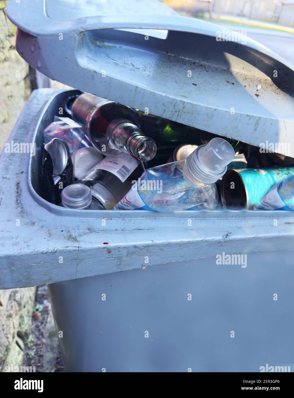 Une poubelle extérieure avec un couvercle qui ne peut pas se fermer, car la poubelle est pleine au débordement de déchets recyclables de bouteilles en plastique et en verre, et de boîtes de conserve. Banque D'Images