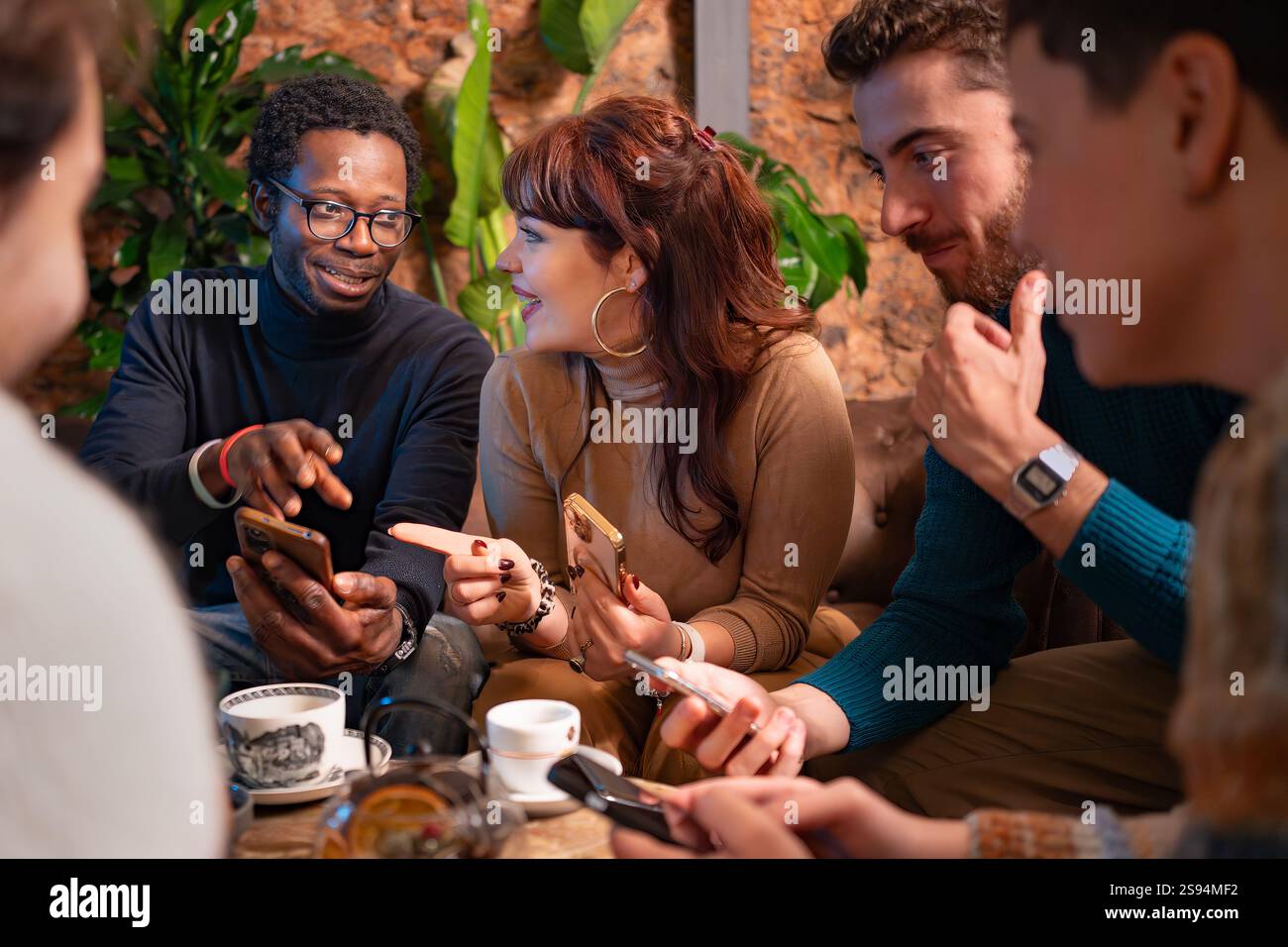Groupe d'amis multiraciaux profitant d'une conversation animée et utilisant des smartphones dans un café confortable. Une atmosphère chaleureuse et accueillante mettant l'accent sur connecti Banque D'Images