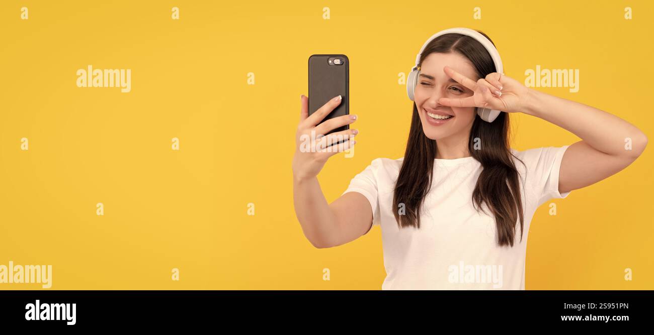 femme positive en chemise blanche dans le casque faisant selfie sur le téléphone avec le geste de paix, selfie. Femme isolée visage portrait, bannière avec espace de copie. Banque D'Images