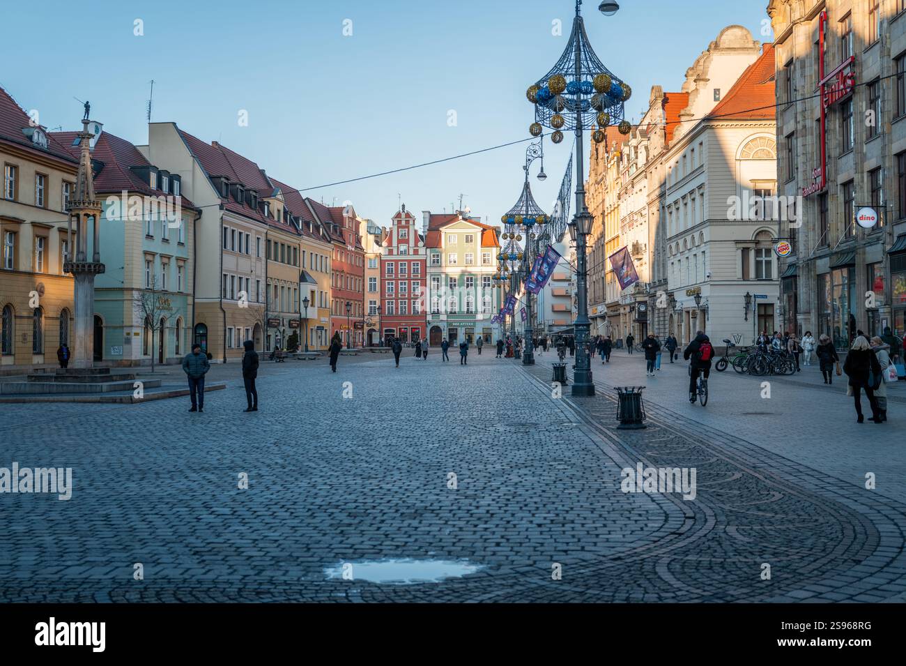 Rynek Square à Wroclaw, en janvier, avec des bâtiments historiques colorés, des lampadaires décoratifs, un pavé, et des gens marchant et cyclant Banque D'Images