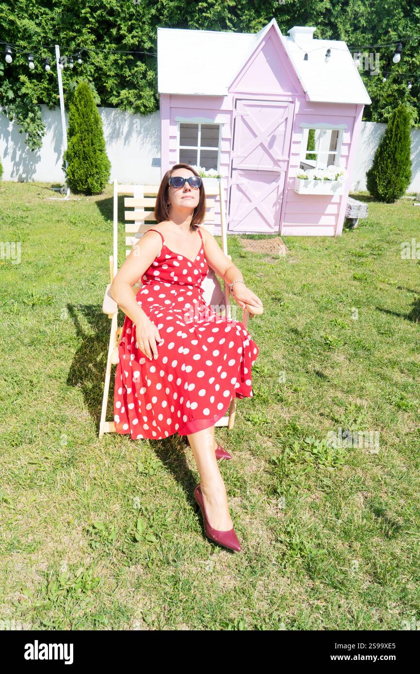 Femme en robe rouge et lunettes de soleil se relaxant à la journée ensoleillée d'été. Banque D'Images Femme en robe rouge et lunettes de soleil se relaxant à la journée ensoleillée d'été. Banque D'Images