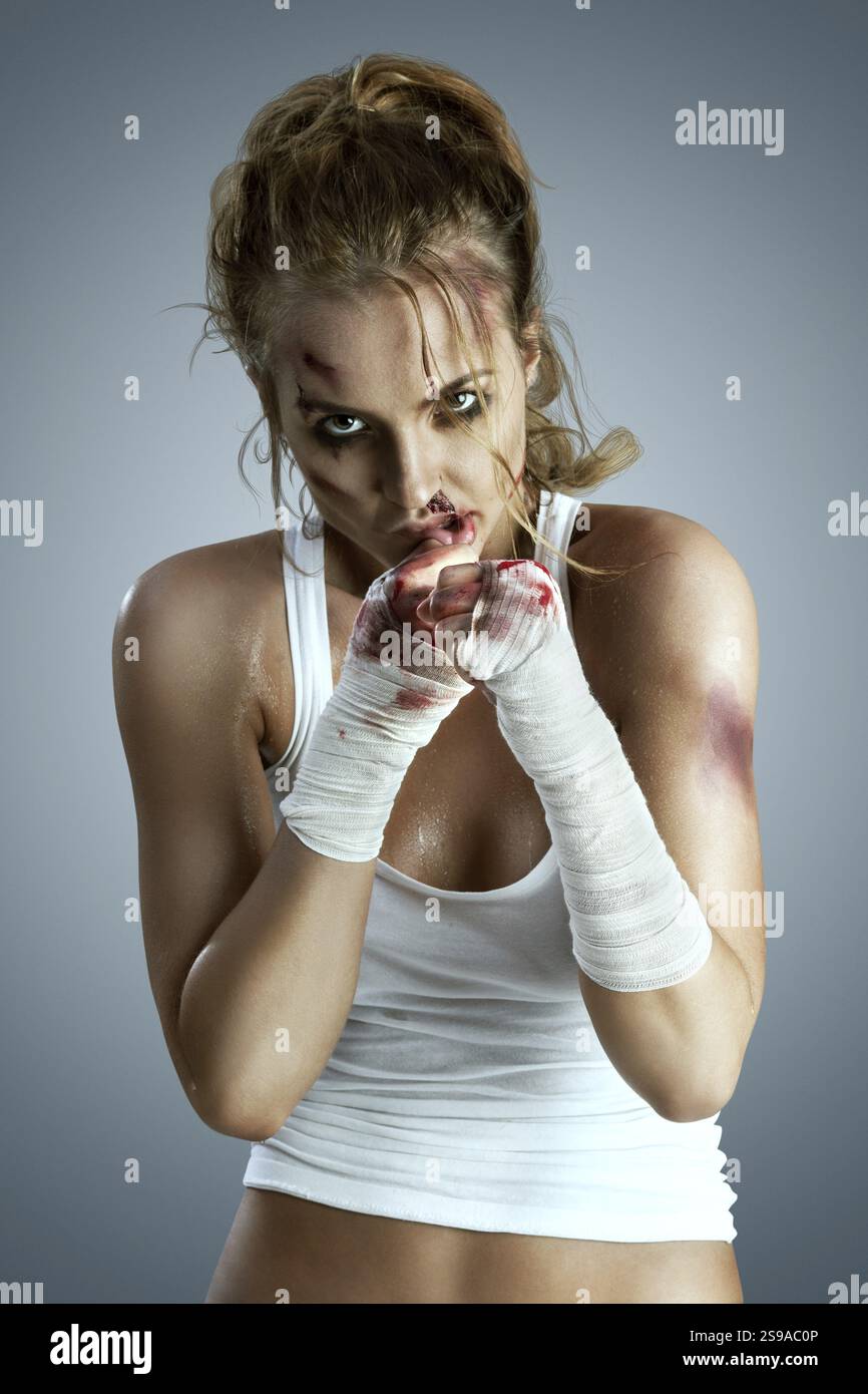 Combattant féminin agressif avec des ecchymoses, portant un bandage sanglant autour de ses poings, debout dans une position de défense de boxe, prête à se battre sur un neutre Banque D'Images