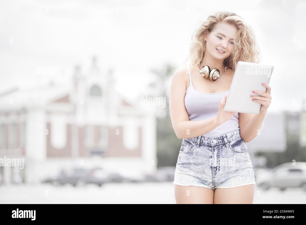Jeune femme heureuse avec des écouteurs vintage autour du cou, surfant sur Internet sur une tablette PC et posant devant un fond urbain Banque D'Images