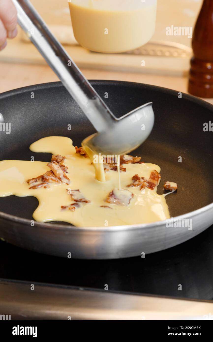 Garnir la pâte aux œufs et au bacon avec garnitures dans une poêle à frire pour la cuisson Banque D'Images