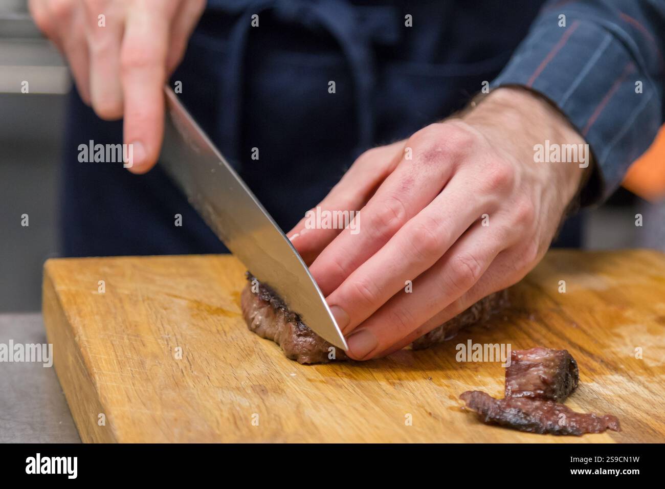 Chef tranchant la viande cuite sur une planche à découper en bois avec couteau pointu, brume Lark Banque D'Images