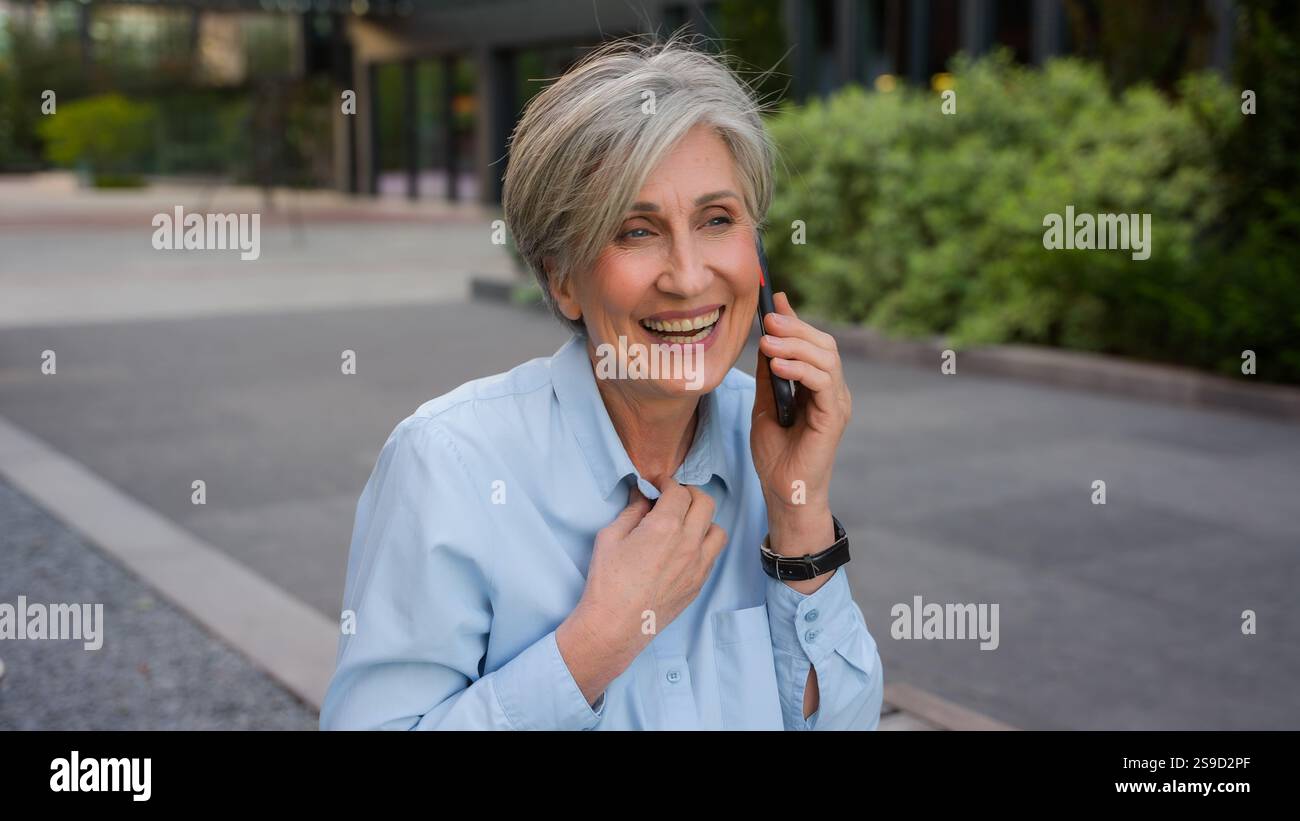 Heureux caucasien émotionnel vieille femme d'affaires senior femme excitée parlant téléphone mobile dans la ville appel smartphone rire agréable distant Banque D'Images