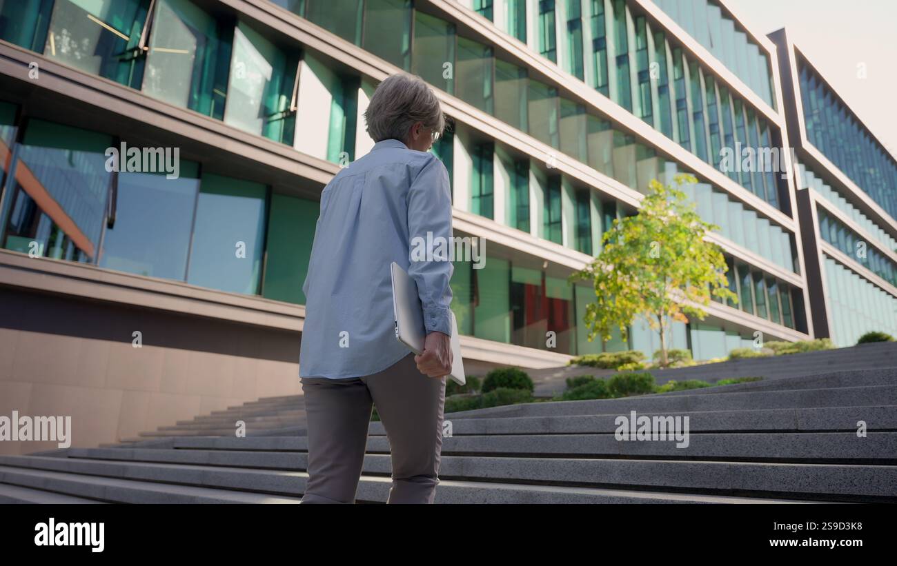 Vue arrière vieille femme aux cheveux gris femme d'affaires marchant jusqu'à l'escalier de l'extérieur à l'immeuble de bureaux moderne méconnaissable femme d'affaires marcher à l'extérieur Banque D'Images