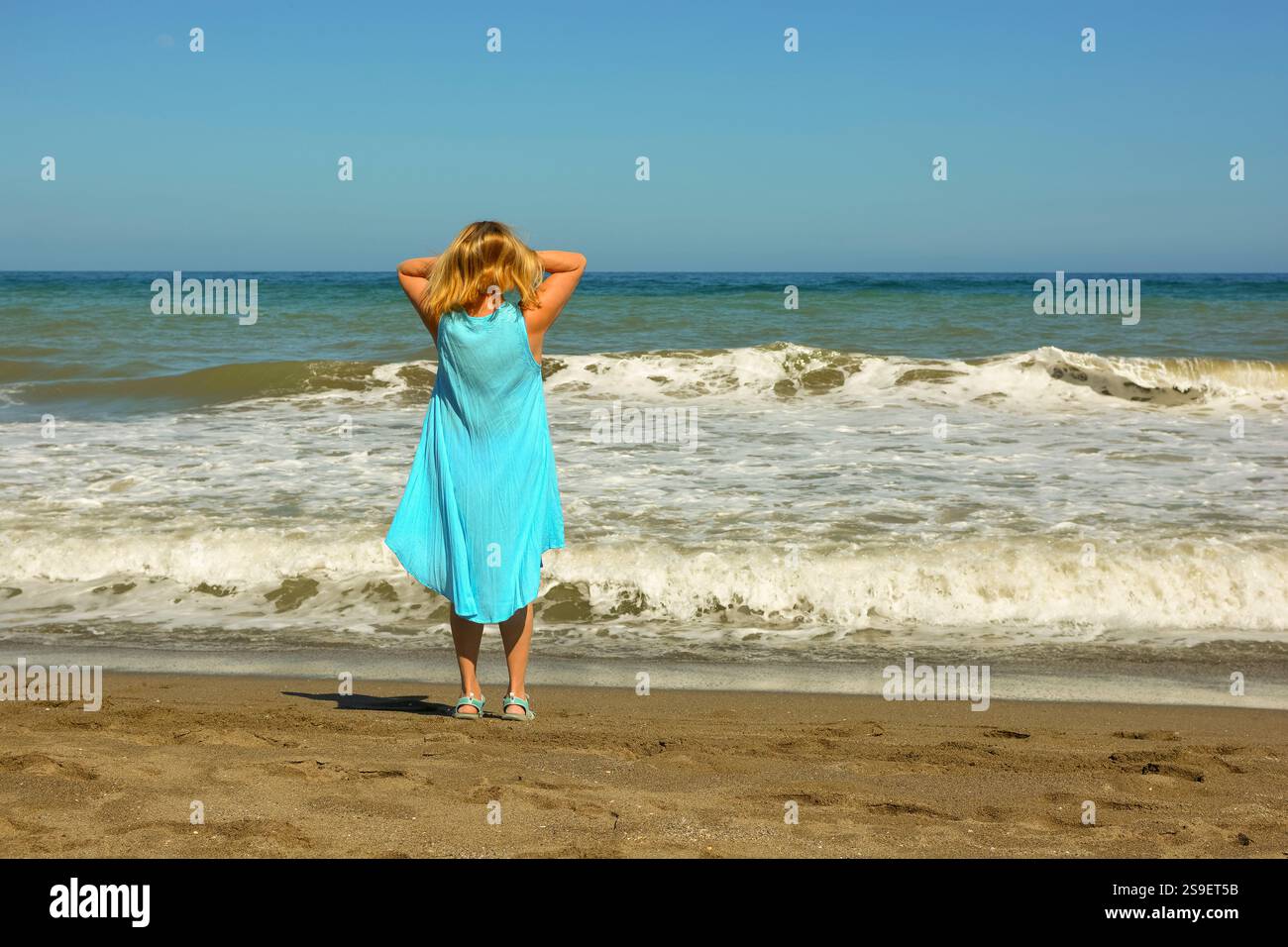 Femme debout sur la plage dans une robe bleue regardant vers la mer Banque D'Images