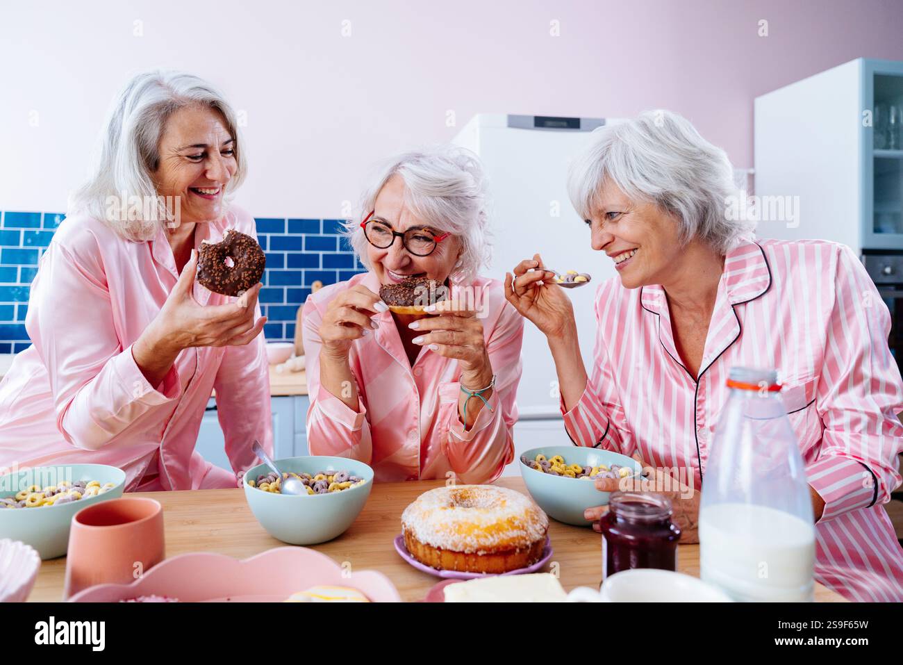 Belles femmes âgées ayant une fête de pyjama drôle à la maison - Groupe d'amies âgées joyeuses s'amusant à la maison et la cuisson dans la cuisine, conc Banque D'Images