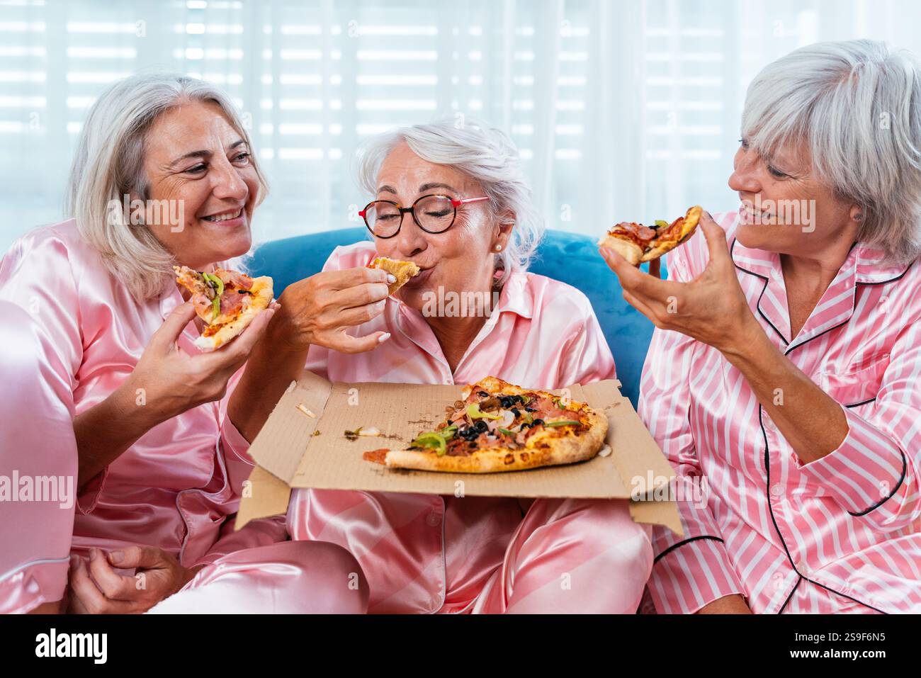 Belles femmes âgées ayant une fête de pyjama drôle à la maison - Groupe d'amies âgées joyeuses s'amusant à la maison manger de la pizza, des concepts sur ol Banque D'Images
