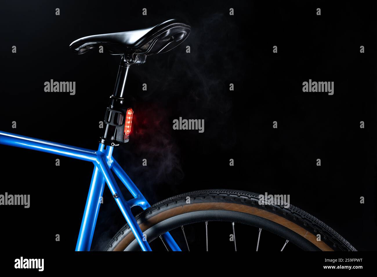Vélo de gravier bleu avec éclairage de clignotant arrière rouge, sécurité cycliste et design élégant sur fond sombre avec fumée blanche Banque D'Images
