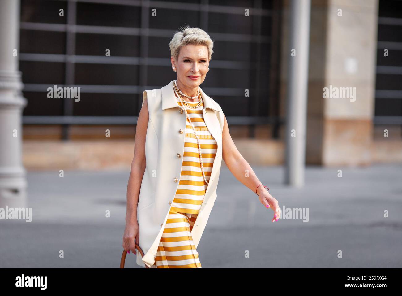 Femme d'affaires mature élégante avec les cheveux courts en gilet blanc élégant Workwear, pantalon rayé jaune et blanc et collier de perles marchant à l'extérieur dans CIT Banque D'Images