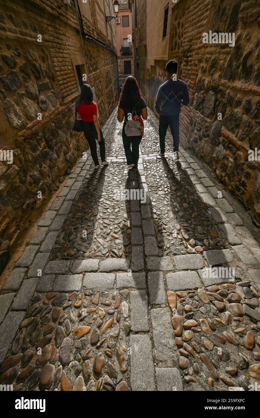 Des personnages rétro-éclairés marchent dans une rue médiévale étroite dans la ville de Tolède, classée au patrimoine mondial de l'UNESCO, en Espagne, Banque D'Images