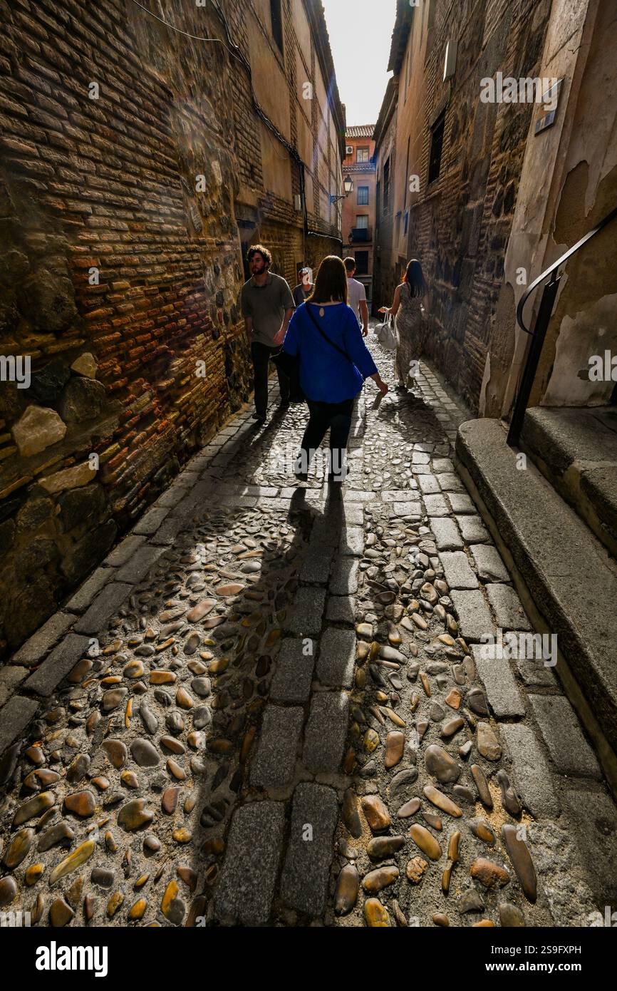 Des personnages rétro-éclairés marchent dans une rue médiévale étroite dans la ville de Tolède, classée au patrimoine mondial de l'UNESCO, en Espagne, Banque D'Images