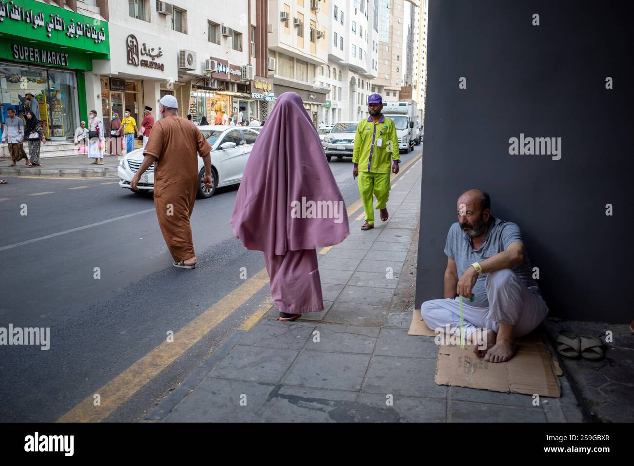 La Mecque, Arabie Saoudite - 13 juin 2024 : personnes assises et marchant près de l'autoroute à Makkah, Arabie Saoudite. Hajj 2024. Banque D'Images
