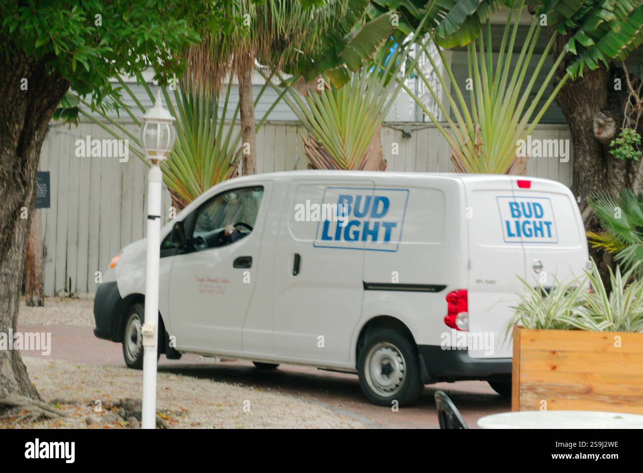 Fourgon blanc de vision large fourgon de livraison Bud Light tirant hors d'une allée avec un lampadaire blanc. Plantes vertes, boîte en bois et arbres. Usage éditorial exclusif Janu Banque D'Images