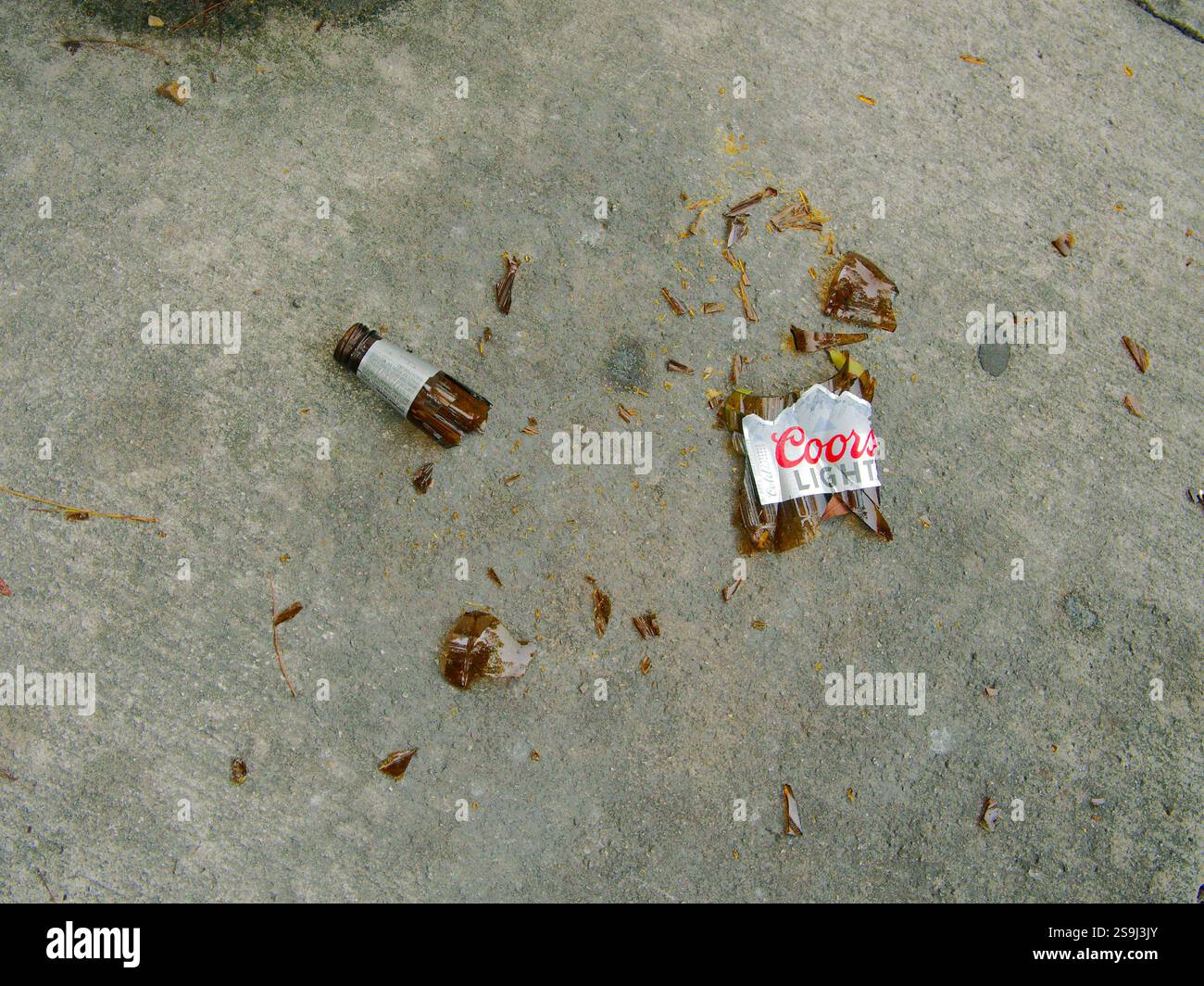 Fermer vue de dessus d'une bouteille de bière Coors Light en verre brun brisé sur un trottoir en béton. Étiquette de goulot et de goulot de bouteille avec morceaux. Utilisation éditoriale sur Banque D'Images