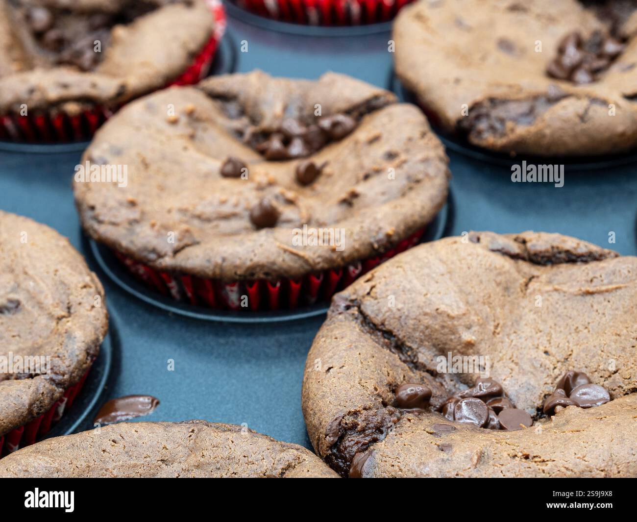 Une vue rapprochée de brownies au chocolat riches et fugaces nichés dans des formes de papier rouge vif, reposant sur une plaque de cuisson, mettant en valeur leur texture irrésistible Banque D'Images