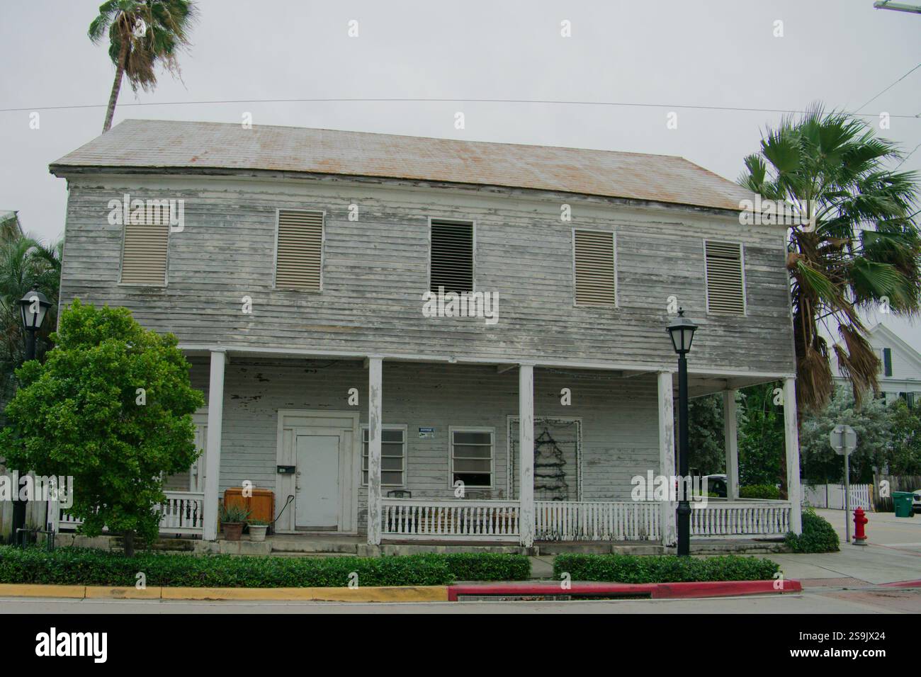 Vieille maison de deux étages en bois vieilli avec une grande enveloppe autour du porche avant. Qu'est-ce que le toit en étain.bouche d'incendie sur la droite. Palmiers et buissons verts an Banque D'Images