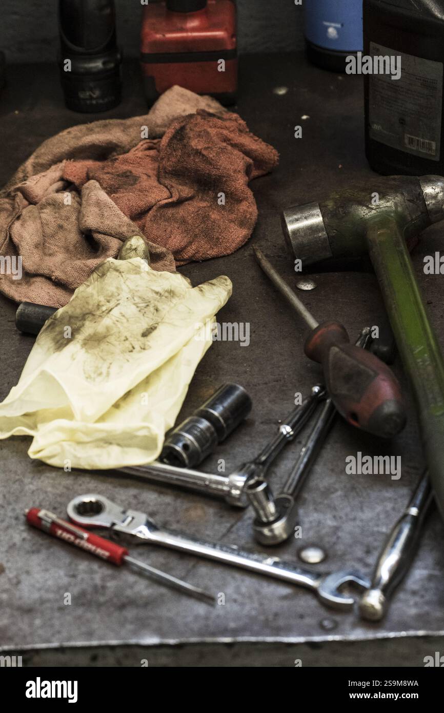 boîte à outils de mécanicien graisseux comprenant des chiffons, des clés, un marteau, un jeu de douilles et des tournevis sur le sol d'un garage en service Banque D'Images