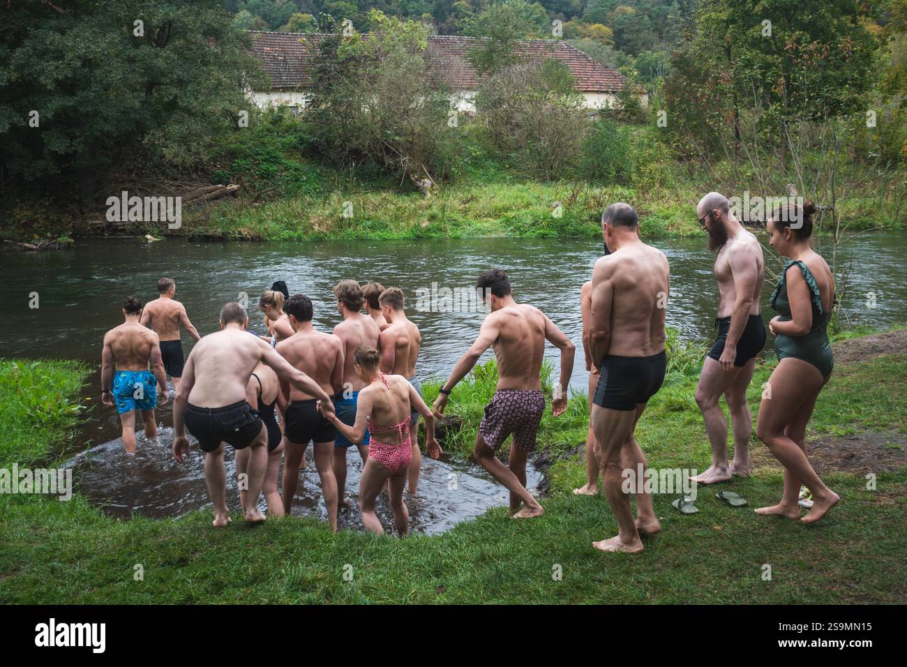 Groupe de personnes en cercle glace se baignant ensemble dans l'eau froide d'une rivière dans une forêt. Méthode Wim Hof, thérapie froide, techniques respiratoires, yoga Banque D'Images