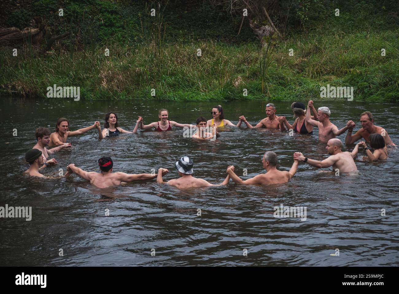 Groupe de personnes en cercle glace se baignant ensemble dans l'eau froide d'une rivière dans une forêt. Méthode Wim Hof, thérapie froide, techniques respiratoires, yoga Banque D'Images