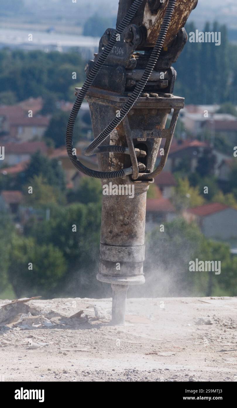 Marteau hydraulique en action lors de la démolition d'un bâtiment. En arrière-plan une zone résidentielle. Banque D'Images