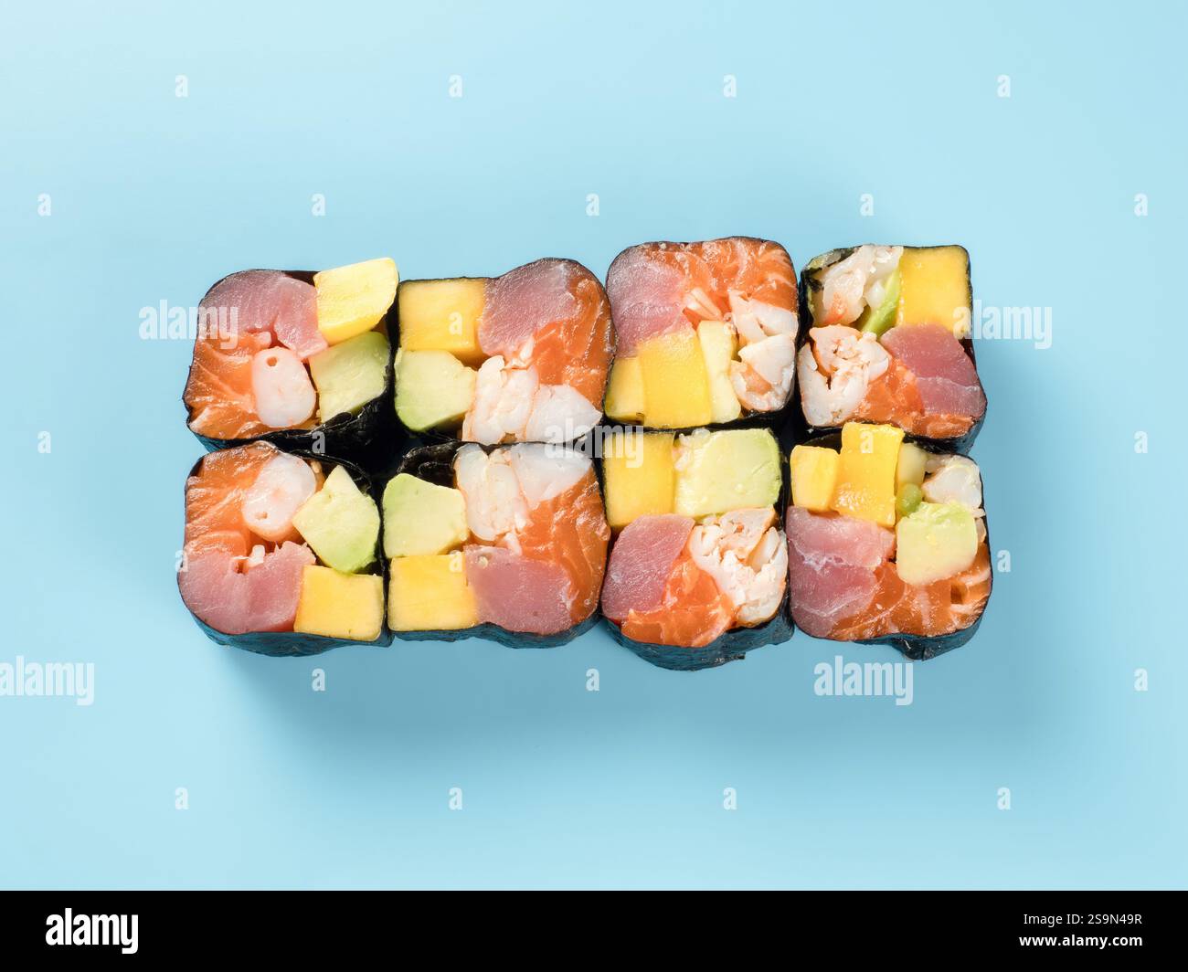 Vue de dessus du rouleau hawaïen avec mangue, avocat, crevette, saumon et thon. Photographie en studio d'un rouleau maki hawaïen coloré avec des crevettes, du saumon et du thon. Isolé sur fond bleu clair solide. Banque D'Images