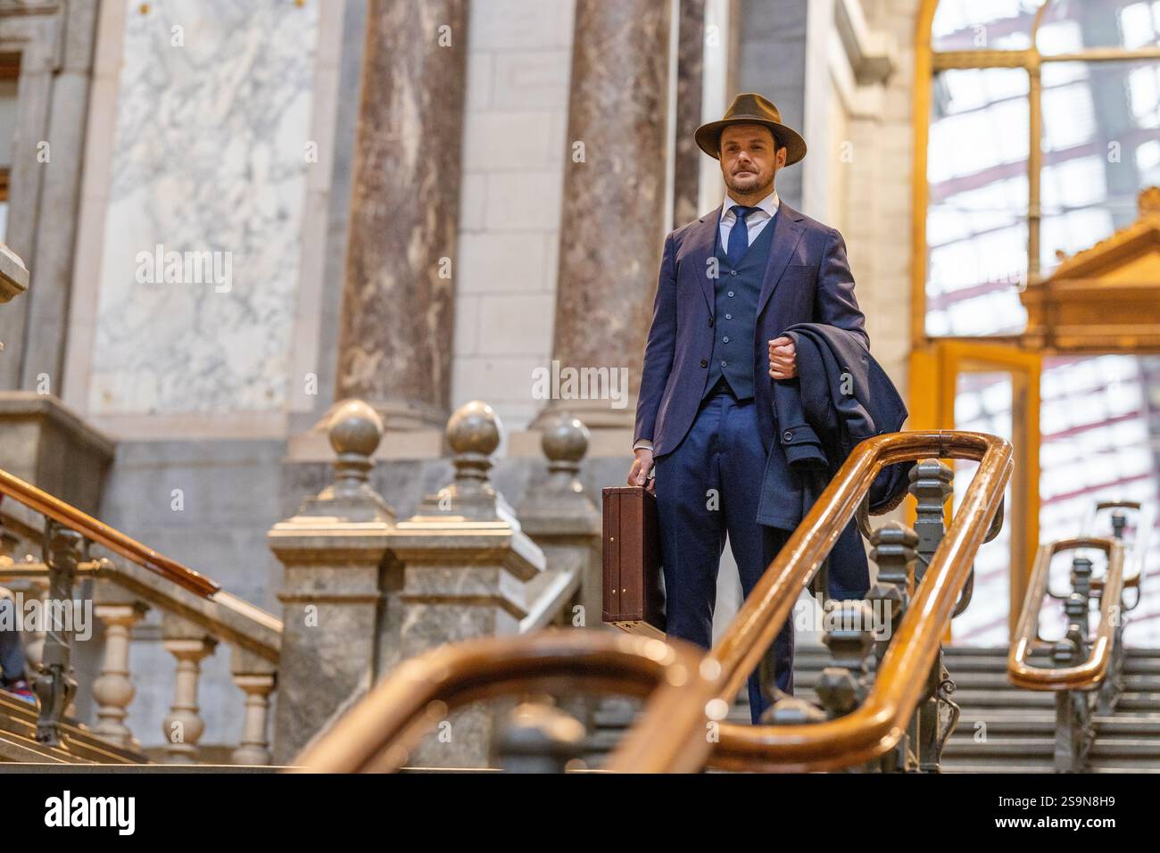 Voyageur descendant escaliers en marbre avec chapeau et porte-documents Banque D'Images