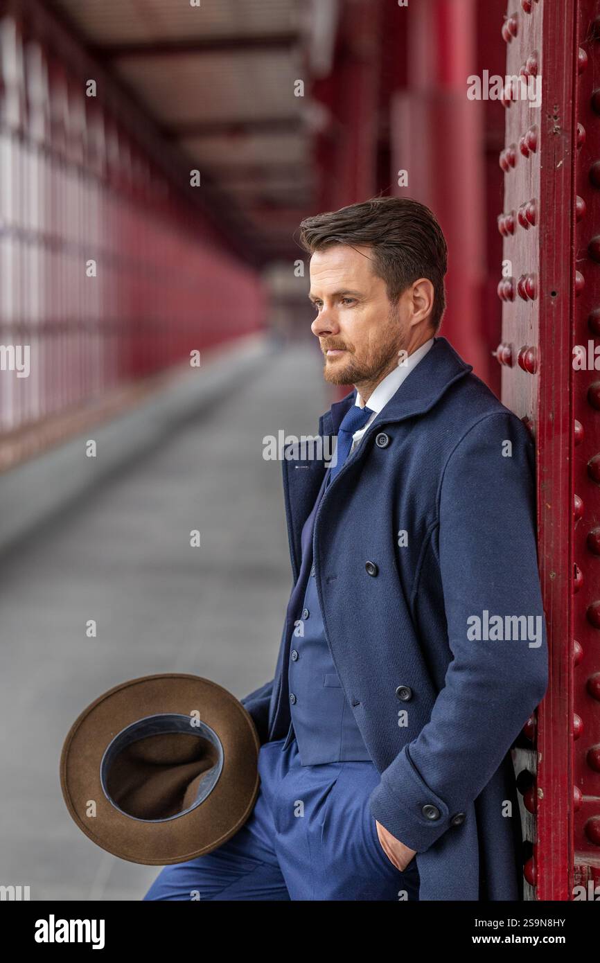 Gentilhomme réfléchi se penchant par la passerelle en costume classique et Fedora Banque D'Images