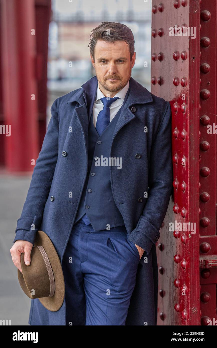 Homme en costume bleu appuyé sur le pilier rouge, tenant le chapeau. Banque D'Images