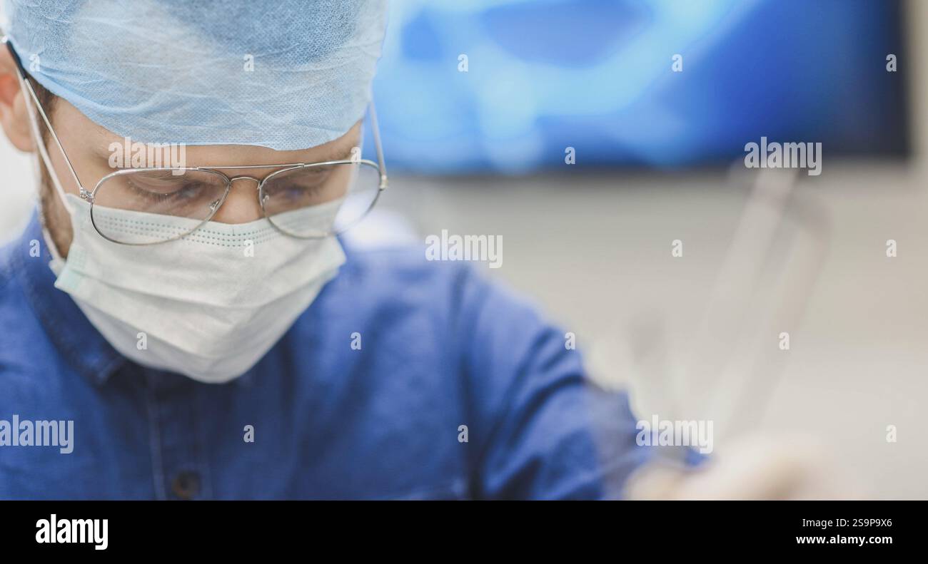 Chirurgien concentré sur la tâche portant un masque, des lunettes et des gommages bleus Banque D'Images