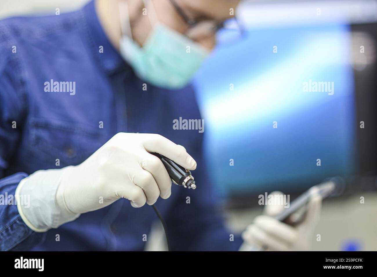Médecin masqué tenant un smartphone et un outil médical, axé sur la tâche dans le cadre de soins de santé Banque D'Images