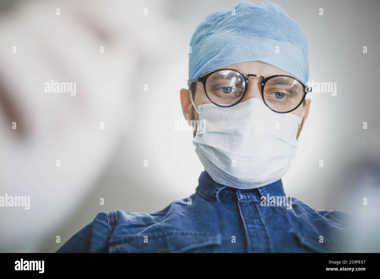 Chirurgien portant une casquette et un masque bleus, axé sur l'exécution d'une tâche médicale Banque D'Images