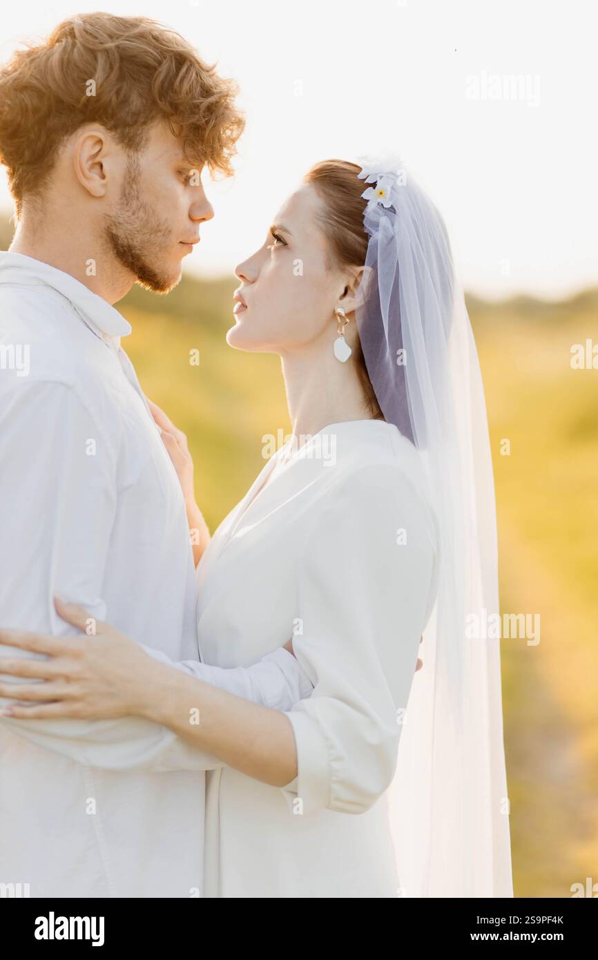 Un couple partageant un moment intime en extérieur dans une tenue de mariage sous la lumière douce du soleil Banque D'Images