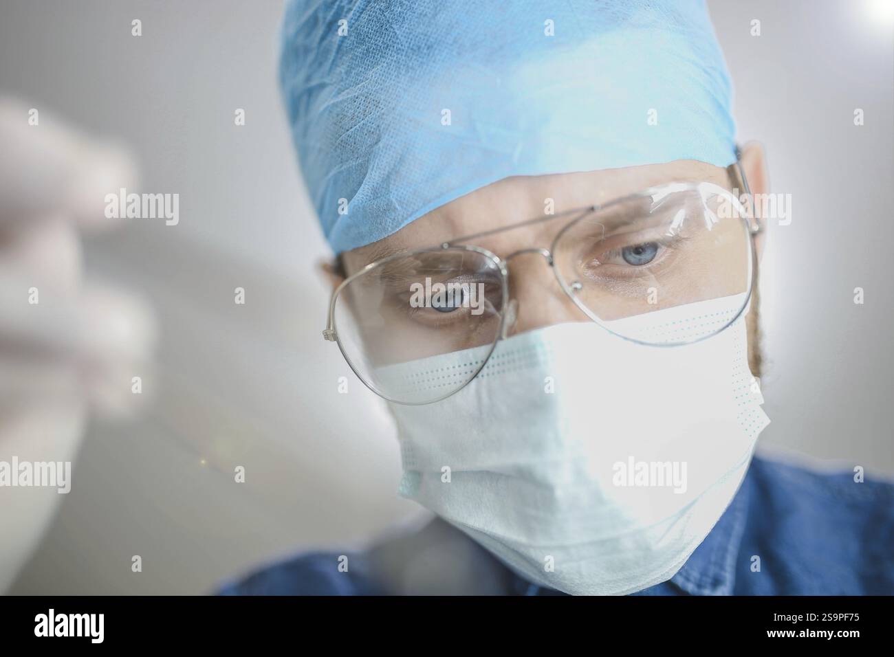 Chirurgien concentré sur une tâche, portant des lunettes et une tenue chirurgicale bleue Banque D'Images