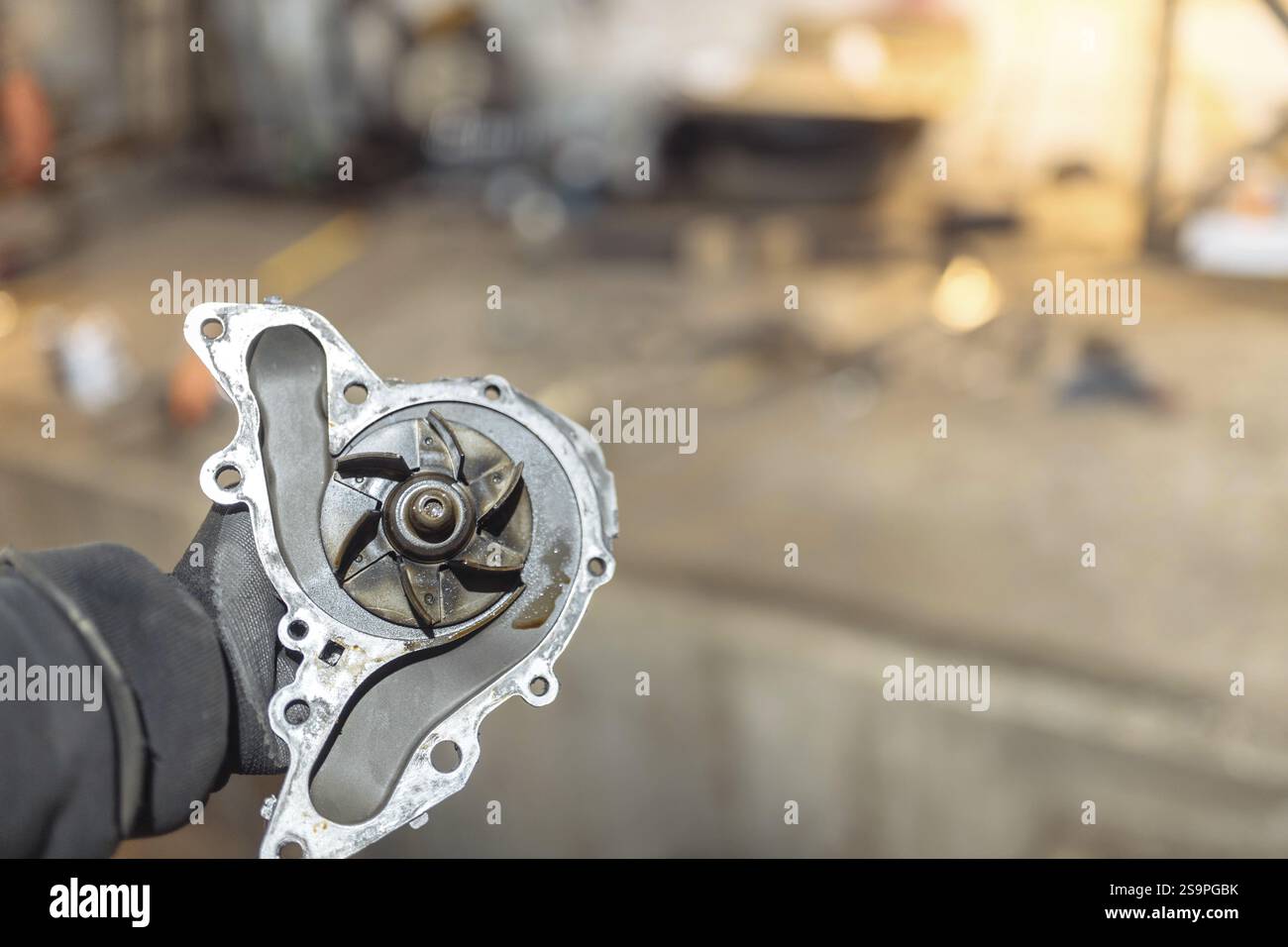 Pièce de voiture en métal tenue à la main, fond d'atelier flou Banque D'Images