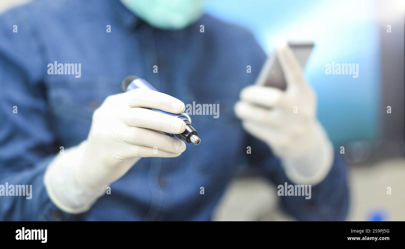 Un professionnel de la santé dans une chemise bleue et des gants tenant un stylo et un smartphone, se concentrant sur la tâche Banque D'Images