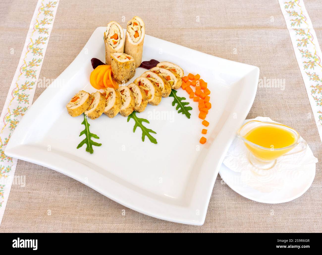 Ce plat gastronomique comprend du poulet roulé fourré de légumes, élégamment plaqué sur un plat blanc. Garnitures vives de carottes, de légumes verts et de sauce enh Banque D'Images