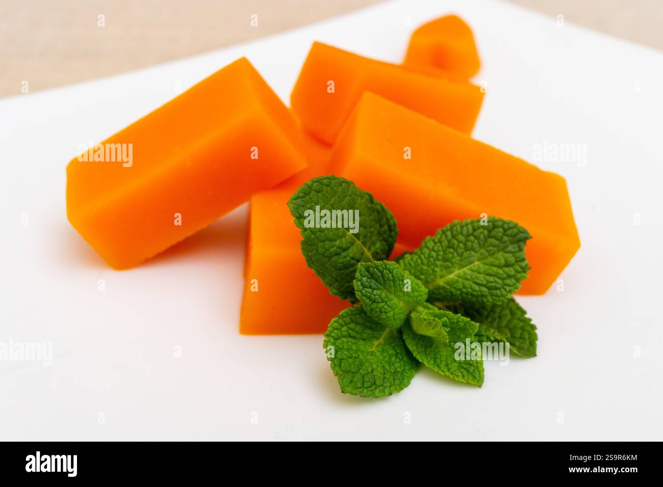 Morceaux de fromage orange éclatants disposés soigneusement sur une assiette blanche, complétés par des feuilles de menthe verte fraîche. La présentation présente un appeti délicieux Banque D'Images