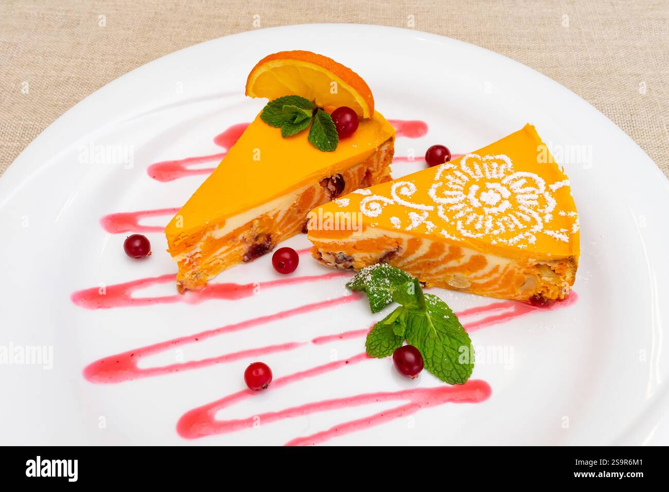 Un dessert vibrant se compose de deux tranches de gâteau aromatisé à l'orange disposées sur une assiette blanche. La sauce aux baies vives et les feuilles de menthe améliorent la présentation, Banque D'Images