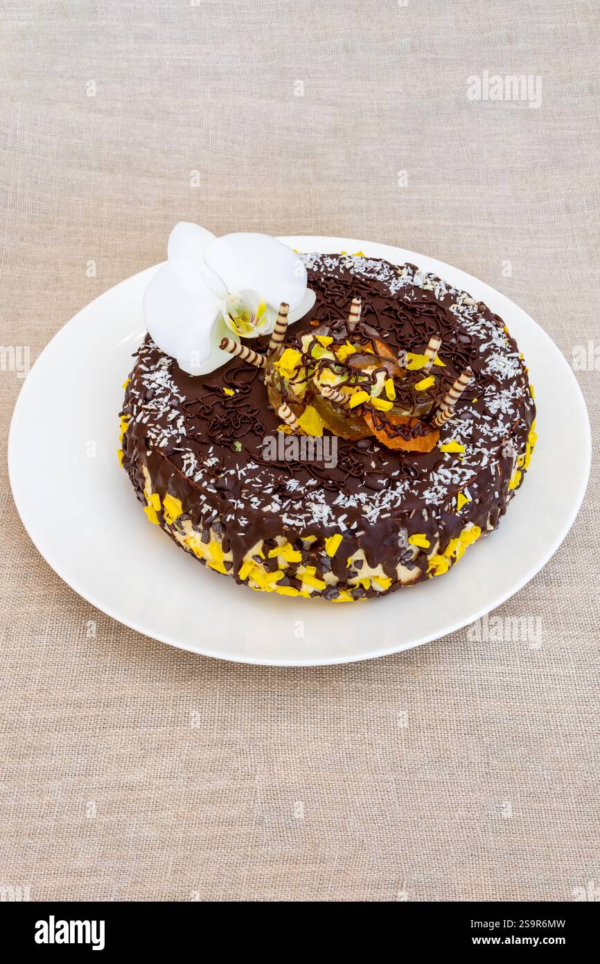 Un gâteau au chocolat magnifiquement décoré se trouve sur une assiette blanche, orné d'étoiles jaunes et de noix de coco râpée. Une fleur d'orchidée blanche améliore l'elega Banque D'Images