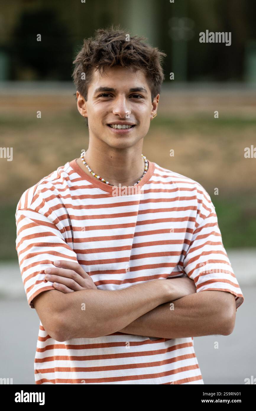 Jeune gars confiant regardant la caméra avec les bras croisés.adolescent satisfait debout détendu dehors et souriant. Banque D'Images