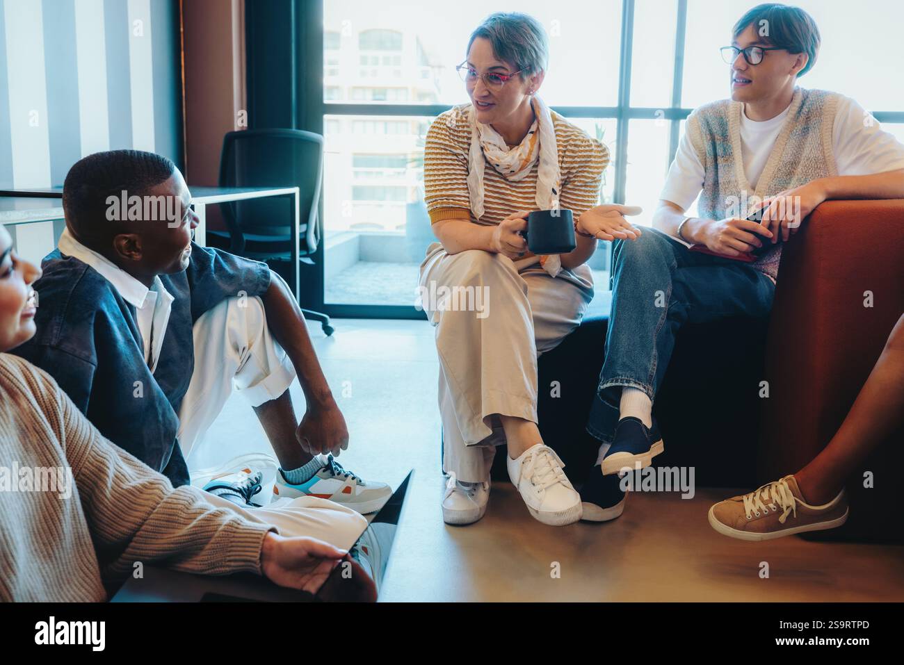 Enseignant parlant avec les élèves dans un cadre décontracté, favorisant la communication et l'engagement lors d'une discussion de groupe détendue dans un classroo contemporain Banque D'Images