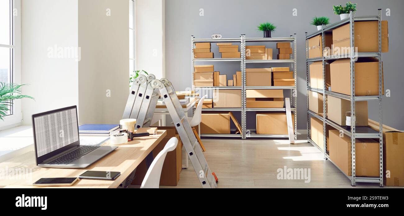 Lieu de travail vide avec bureau et ordinateur portable dans l'entrepôt avec des étagères remplies de boîtes en carton Banque D'Images