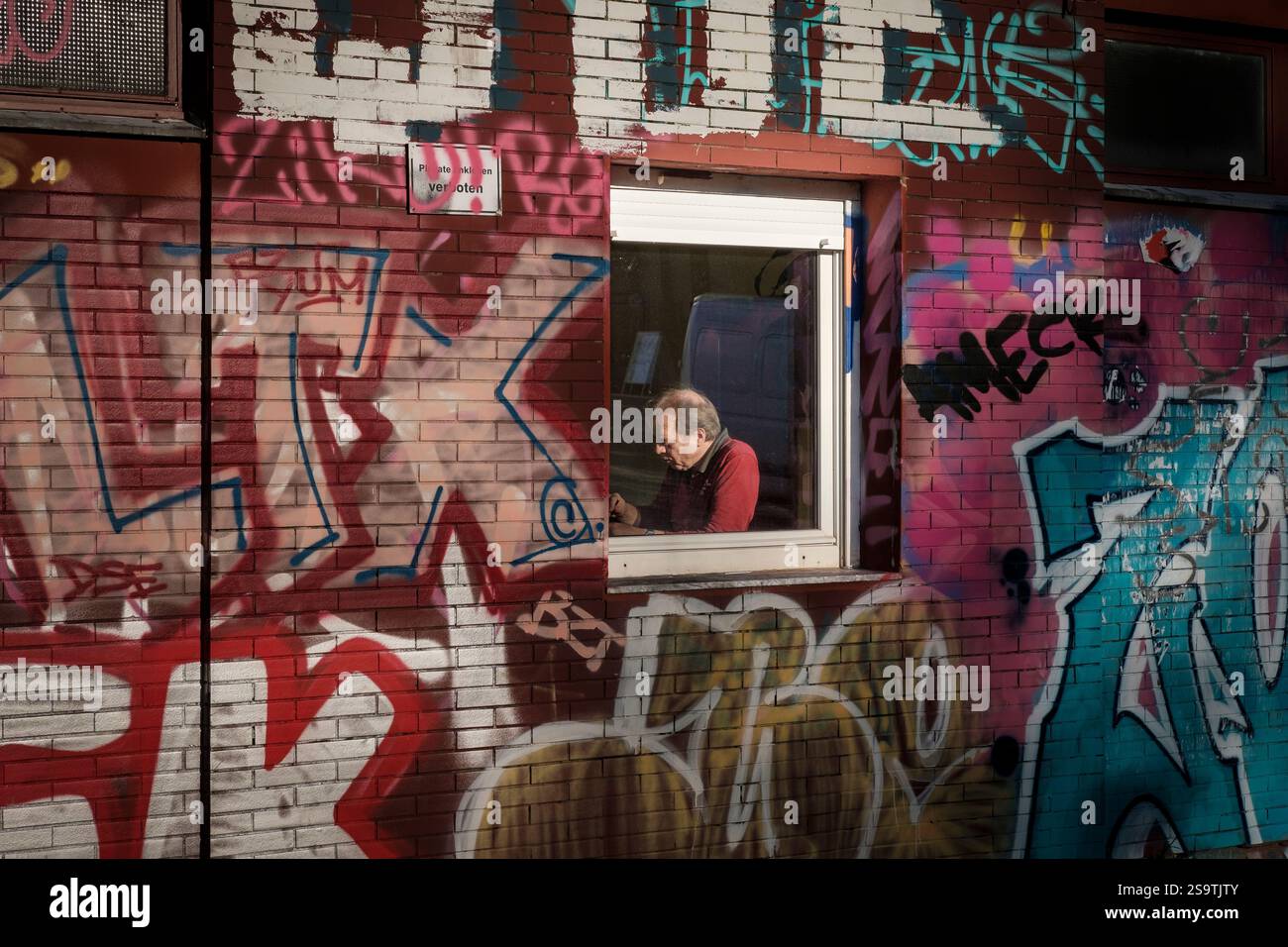 Homme par la fenêtre sur le mur couvert de graffiti, Berlin, Allemagne Banque D'Images