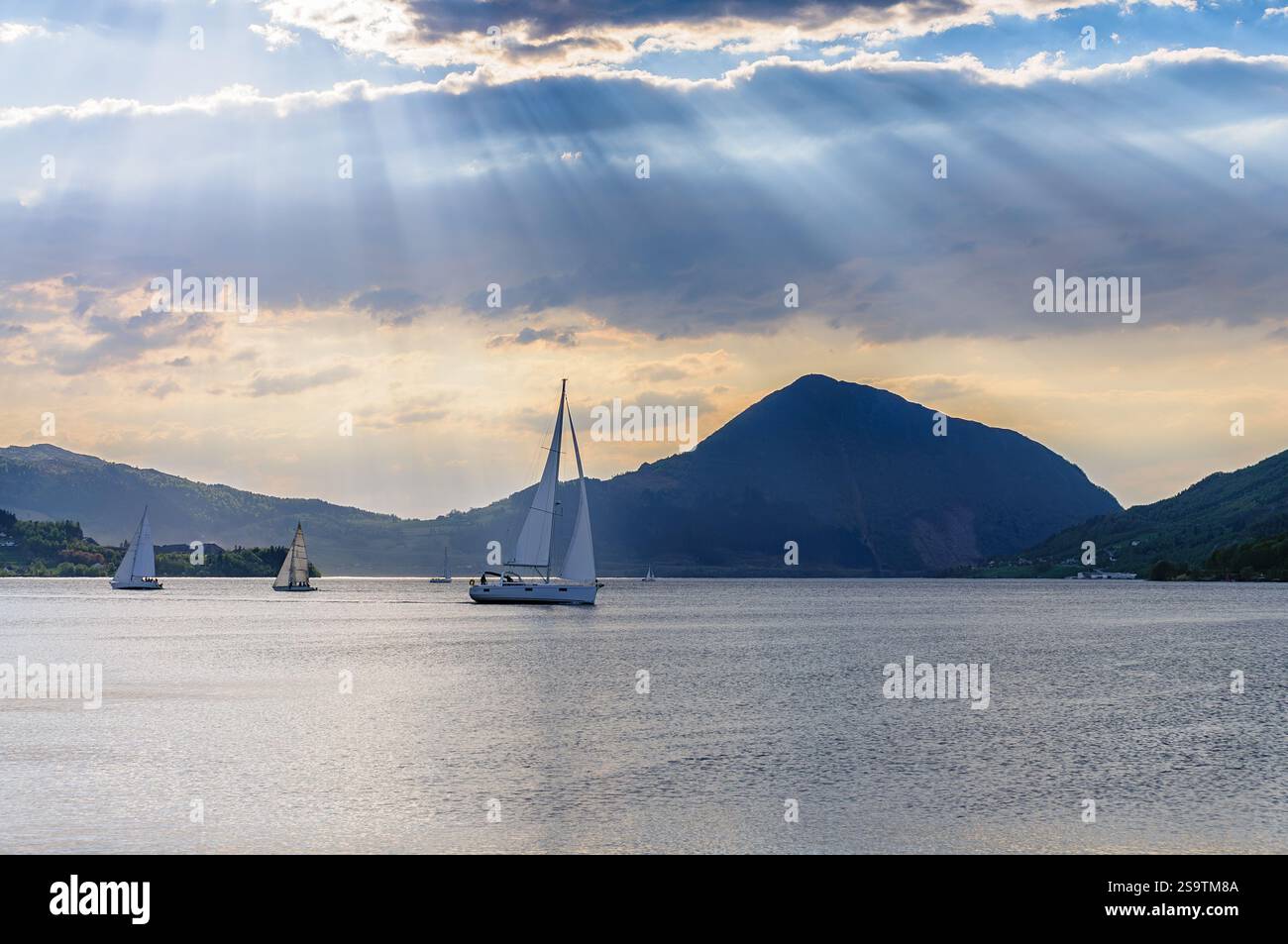Les voiliers naviguent sur les eaux tranquilles de la Norvège alors que le soleil se couche derrière des montagnes majestueuses, créant une atmosphère paisible et enchanteresse. Banque D'Images